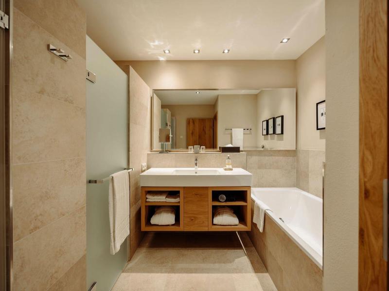 Jasna łazienka z dużą wanną, umywalką, lustrem i jasnymi płytkami.