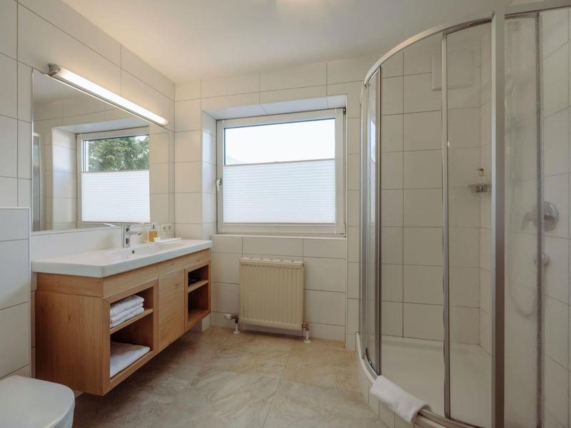 Jasna łazienka z prysznicem, umywalką i oknem w nowoczesnym pokoju hotelowym.