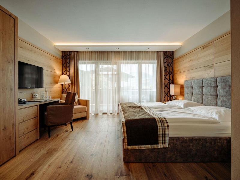 Nowoczesny pokój hotelowy z podwójnym łóżkiem, biurkiem, telewizorem i dużym oknem z zasłonami.