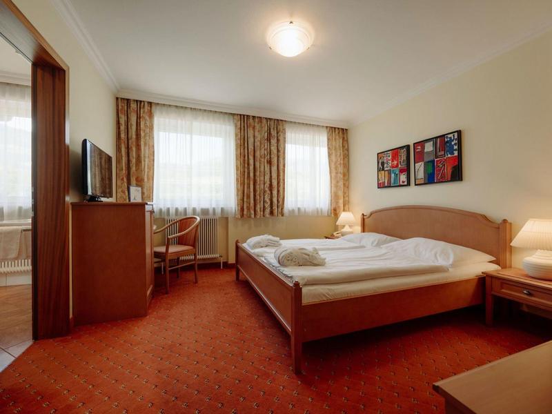 Przytulny pokój hotelowy z podwójnym łóżkiem, biurkiem, telewizorem i ciepłym dywanem.