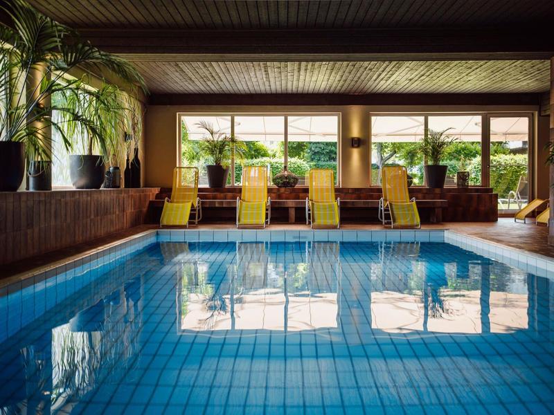 Basen kryty z niebieskimi płytkami i miejscami do siedzenia obok dużych okien w hotelu.