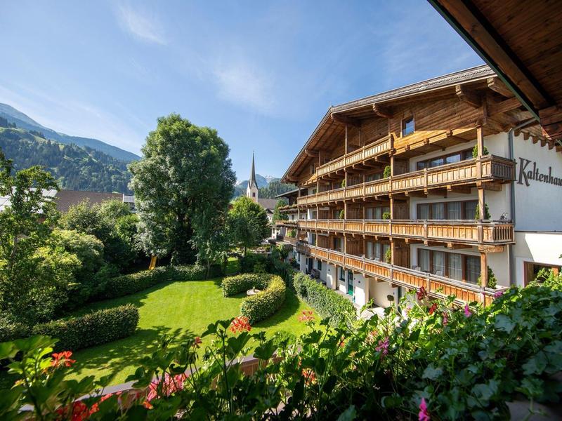 Hotel z pokojami z balkonem obok zielonego ogrodu i gór w tle pod niebieskim niebem.