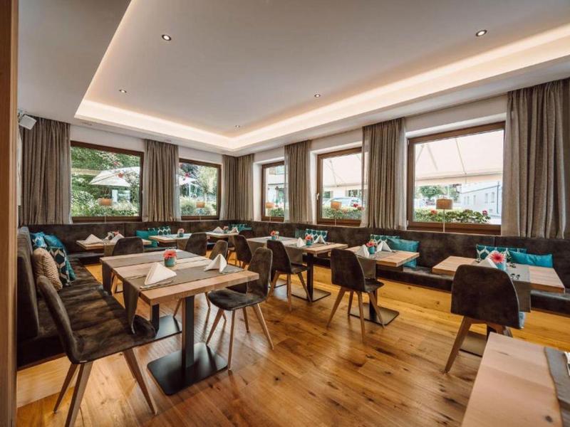 Przytulna sala jadalna hotelu z drewnianą podłogą, ławkami i dużymi oknami z widokiem na góry.