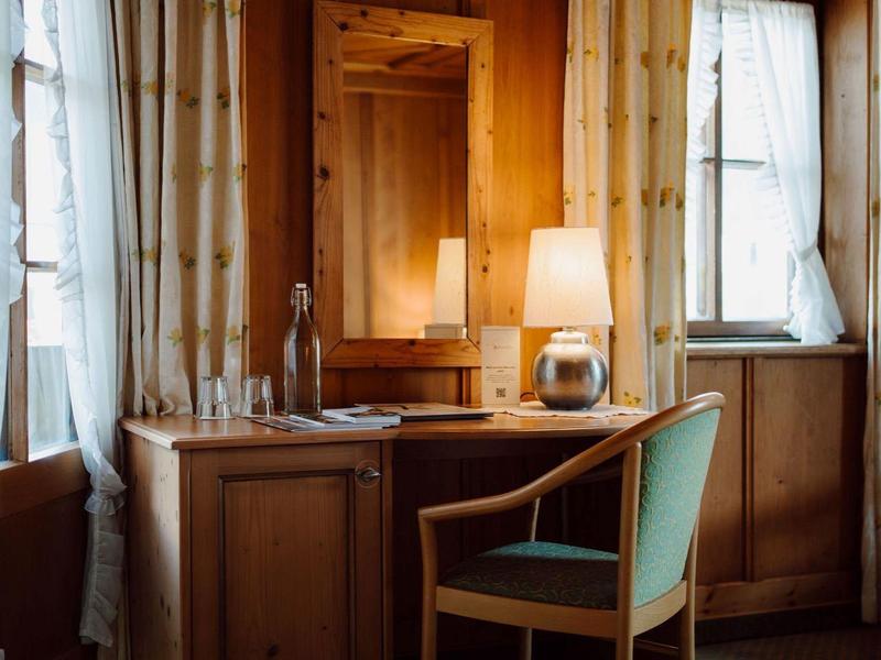 Drewniane biurko z krzesłem, lampą i lustrem między dwoma oknami w przytulnym pokoju hotelowym.