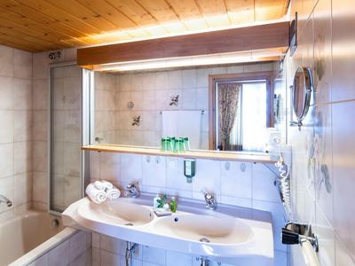 Jasno oświetlona łazienka z wanną, podwójną umywalką i dużym lustrem w pokoju hotelowym.