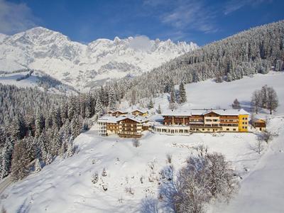 Hotel op sneeuwbedekte berg met uitzicht op besneeuwde dennenbomen en bergtoppen onder een blauwe lucht.