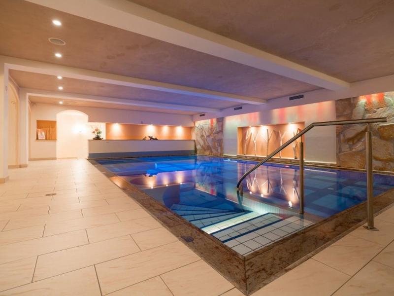 Nowoczesny kryty basen ze schodami, jasnymi kafelkami i oświetleniem pośrednim w hotelu.