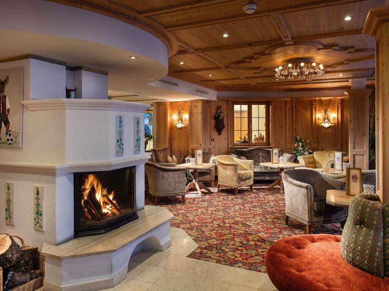 Przytulny salon hotelowy z otwartym kominkiem, drewnianą boazerią i wygodnymi fotelami.