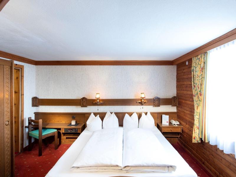 Przytulny pokój hotelowy z podwójnym łóżkiem, światłem dziennym z okien z zasłonami i ciepłymi drewnianymi akcentami.