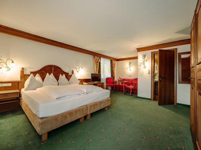 Przytulny pokój hotelowy z dużym łóżkiem, zielonym dywanem i częścią wypoczynkową z czerwonymi fotelami.