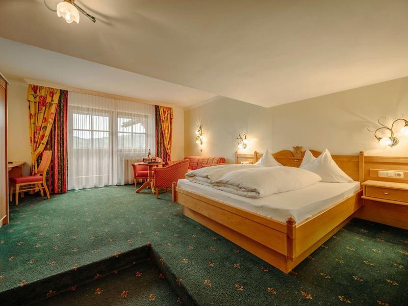 Jasny pokój hotelowy z łóżkiem podwójnym, zielonym dywanem, czerwonymi zasłonami i miejscem do siedzenia przy oknie.