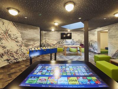 Modern hotel lounge area with TV, foosball table, colorful seating, and interactive floor display.