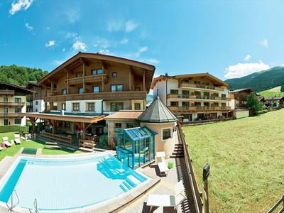Hotel with outdoor pool, sun loungers, and green mountain scenery on a sunny day.