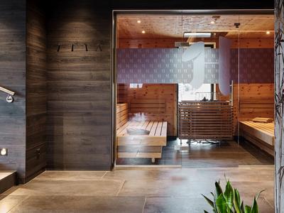 Modern sauna room with wooden benches, glass wall, and plants in the foreground.