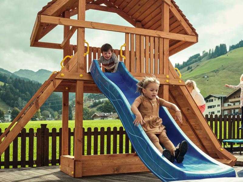 Children playing on a wooden playground with slide in a rural setting.