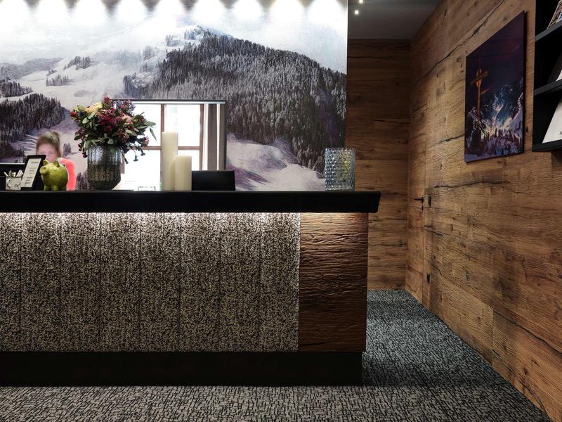 Modern hotel lobby with rustic wooden wall, sleek reception desk, and mountain panorama in the background.