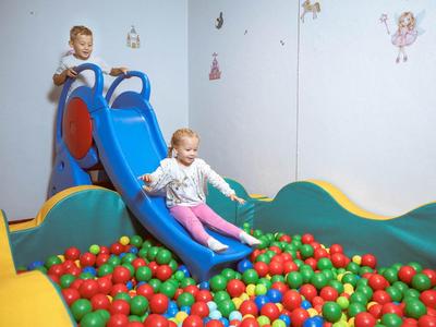 Children slide down a blue slide into a colorful ball pit in the play area.