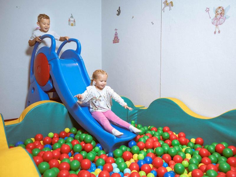 Children slide down a blue slide into a colorful ball pit in the play area.