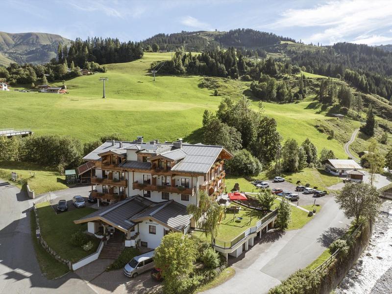 Hotel in green mountain landscape with parking and adjacent meadows under cloudy sky.
