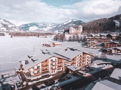Hotelgebäude mit verschneitem Dach in einer winterlichen Berglandschaft mit Bergen im Hintergrund.