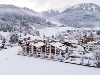 Schneebedecktes Dorf im Tal, umgeben von bewaldeten Bergen und schneebedeckten Gipfeln.