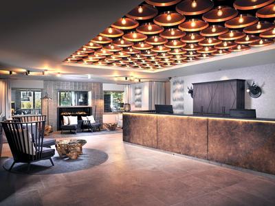 Großzügige Hotel-Lobby mit modernem Tresen, Holzstühlen, Kamin und warmem Deckenlichtdesign.