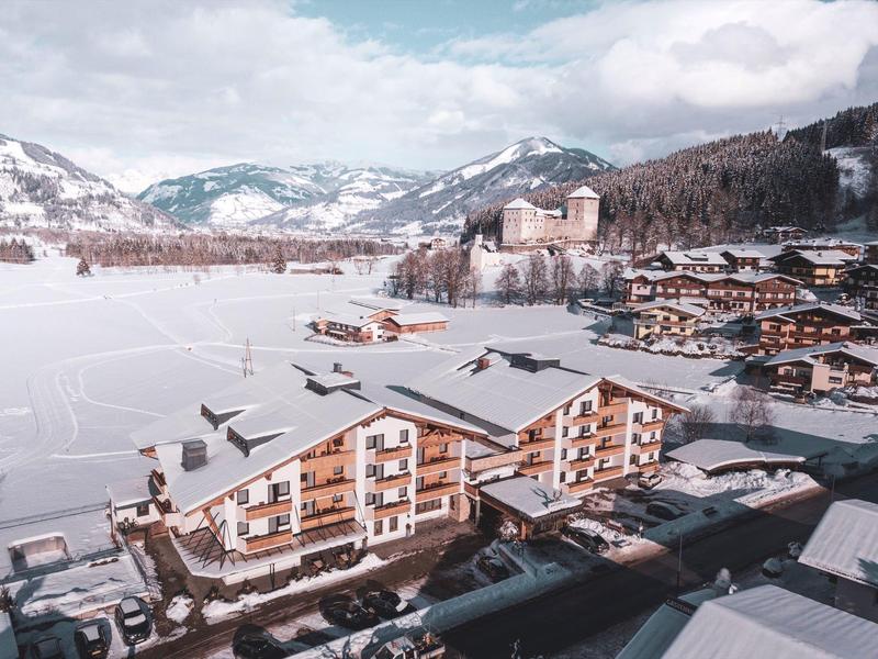 Hotelgebäude mit verschneitem Dach in einer winterlichen Berglandschaft mit Bergen im Hintergrund.