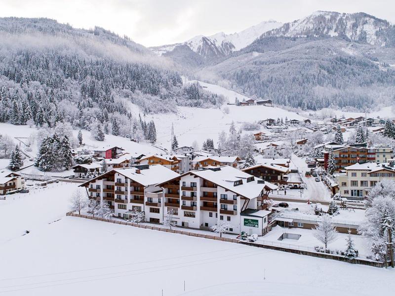 Schneebedecktes Dorf im Tal, umgeben von bewaldeten Bergen und schneebedeckten Gipfeln.