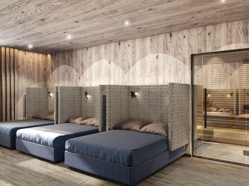 Moderner Schlafraum mit drei Betten, Holzverkleidung und Glastür zu Sauna, warme Beleuchtung.