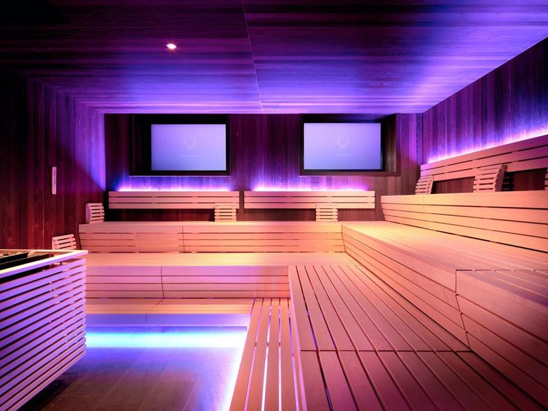 Moderne Sauna mit mehrstufigen Holzliegen und violettem LED-Licht an Decke und Wänden.