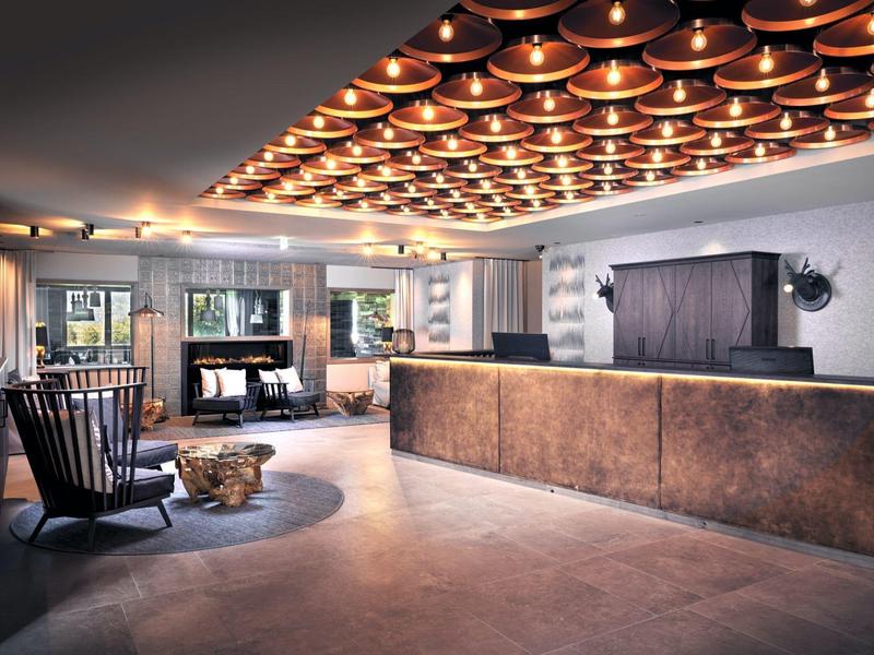Großzügige Hotel-Lobby mit modernem Tresen, Holzstühlen, Kamin und warmem Deckenlichtdesign.