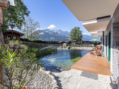 Uitzicht op een modern balkon met berglandschap en heldere vijver bij een rustig hotel.