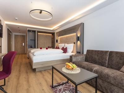 Nowoczesny pokój hotelowy z dużym łóżkiem, sofą, stołem, krzesłem, drewnianą podłogą i oświetleniem pośrednim.