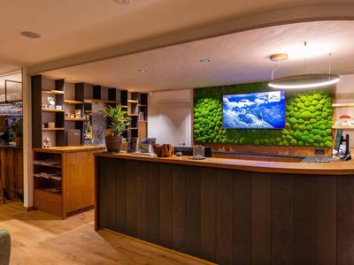 Receptie in een modern hotel met houten meubels en groene mosdecoratie achter de balie.