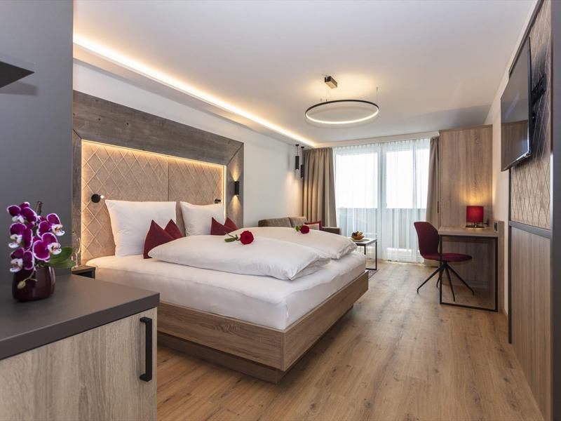 Nowoczesny pokój hotelowy z łóżkiem dwuosobowym, biurkiem, fotelem i dużym oknem.