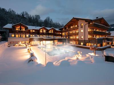 Osvětlený hotel v zimě se sněhem pokrytým venkovním bazénem za soumraku.