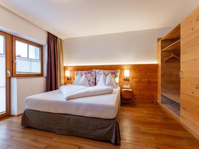 Světý hotelový pokoj s manželskou postelí, dřevěným nábytkem a oknem se závěsy.