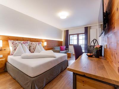 Moderní hotelový pokoj s manželskou postelí, dřevěným dekorem a psacím stolem u okna.