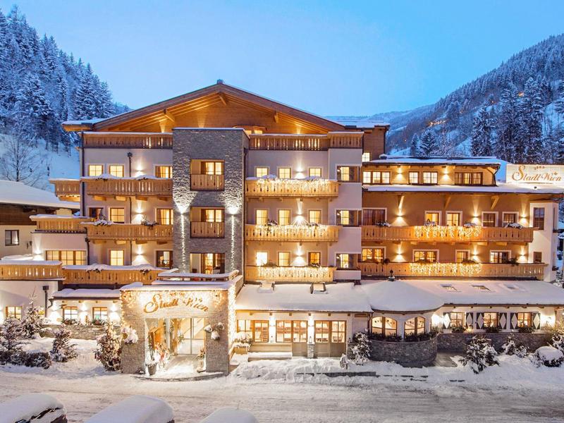 Velká hotelová budova v zasněžených horách za soumraku s osvětlenými okny.