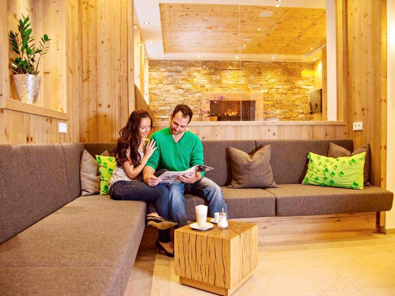 Pár sedí pohodlně na útulné dřevěné pohovce v teple osvětlené místnosti.