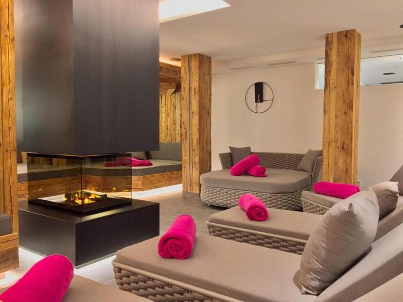 Moderní lounge prostor se šedými pohovkami, růžovými ručníky a centrálním krbem v hotelu.