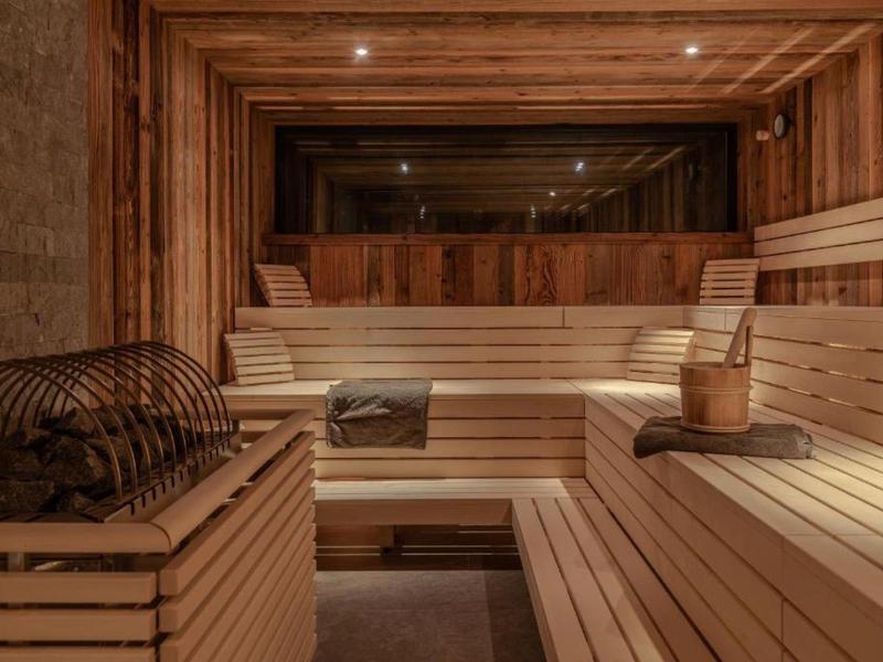 Pohodlná sauna s dřevěnými lavicemi, saunovou kamny a dřevěným kýblem v teplém osvětlení.