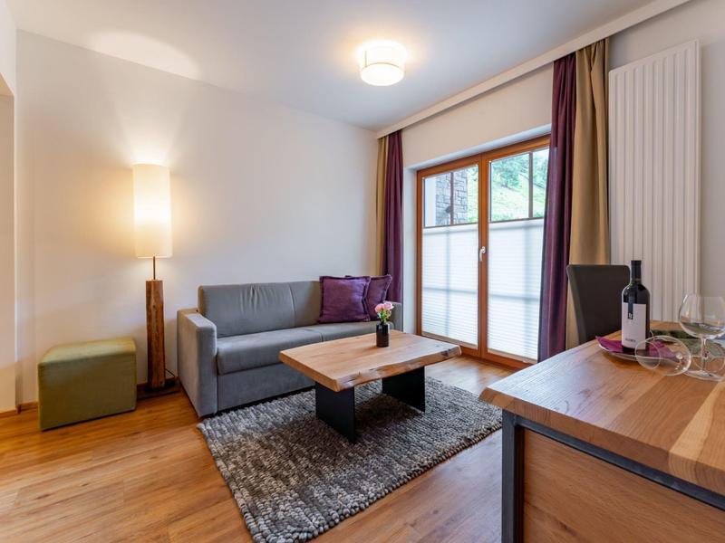 Pohodlný obývací pokoj s pohovkou, konferenčním stolkem, kobercem a velkým oknem se závěsy.