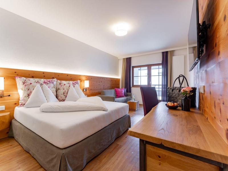 Moderní hotelový pokoj s manželskou postelí, dřevěným dekorem a psacím stolem u okna.