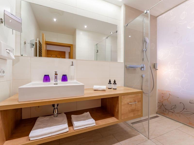 Moderní koupelna se dřevěnou umyvadlovou skříňkou, velkým zrcadlem a skleněným sprchovým koutem s matným sklem.