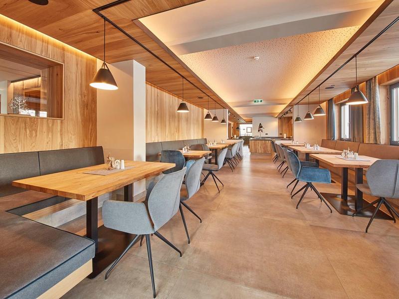 Restaurant moderne avec murs en bois, chaises grises et tables élégantes sous un éclairage chaleureux.