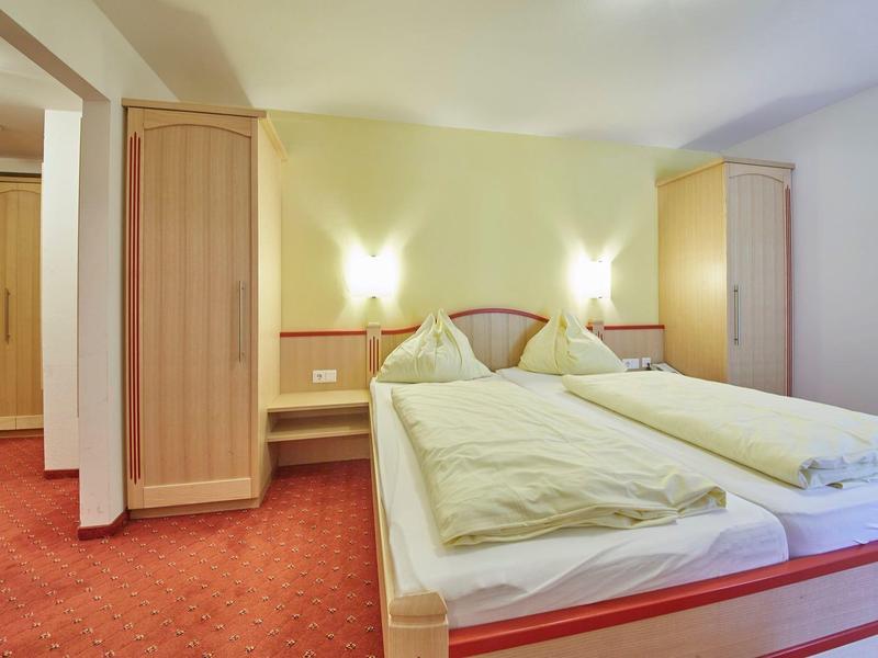 Chambre d'hôtel confortable avec deux lits simples, meubles en bois et moquette rouge.