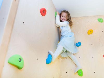Dziecko radośnie wspina się po kolorowej ściance wspinaczkowej w pomieszczeniu.