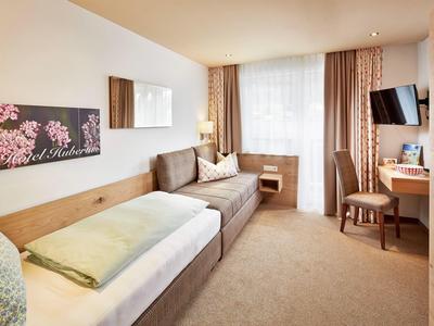 Przytulny pokój hotelowy z pojedynczym łóżkiem, sofą i biurkiem przy dużym oknie.