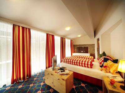 Jasny pokój hotelowy z dużym łóżkiem, pasiastymi zasłonami i przytulnym oświetleniem.